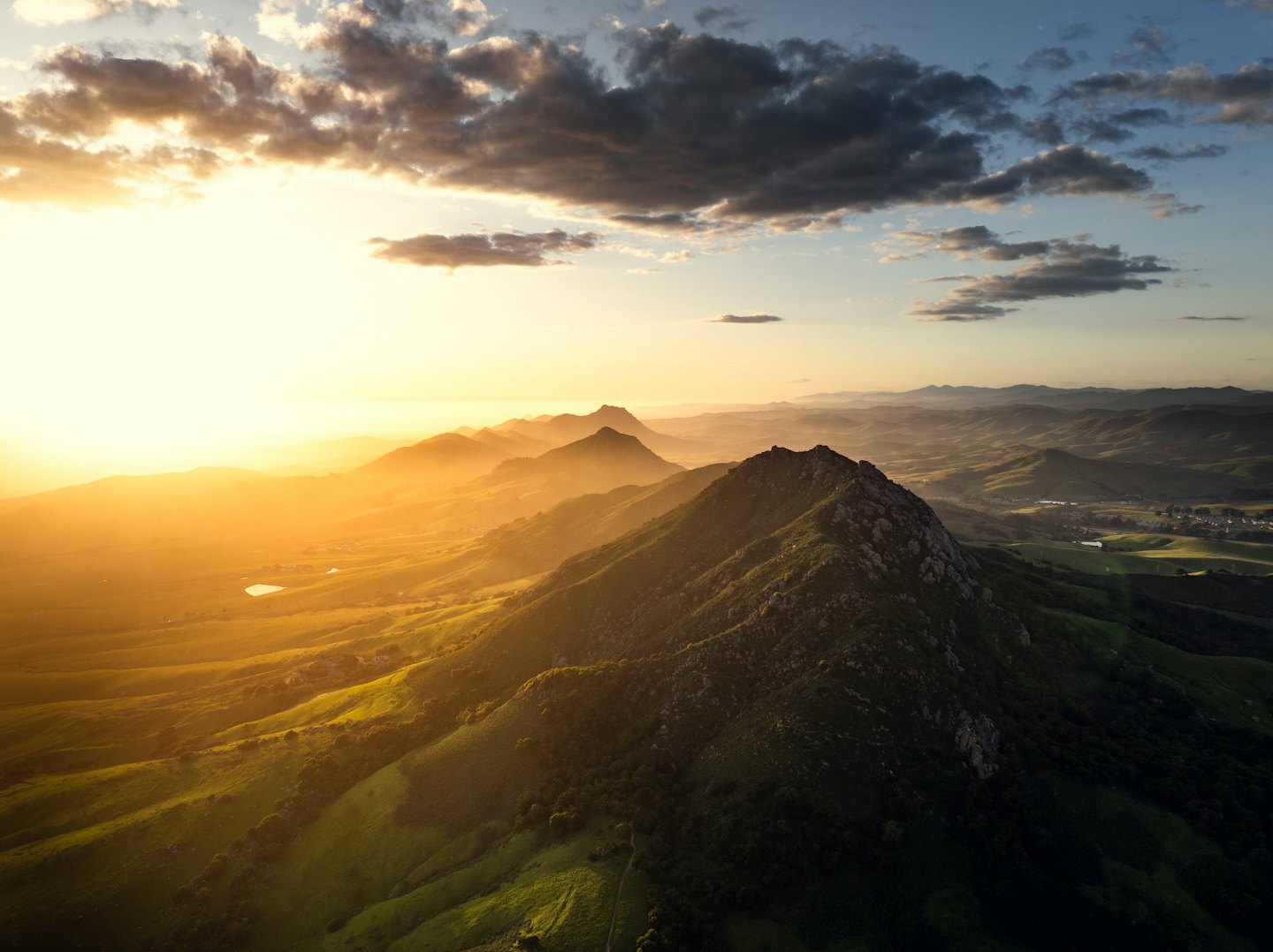 Rolling green mountain hills and rocky peaks under a cloudy sky.