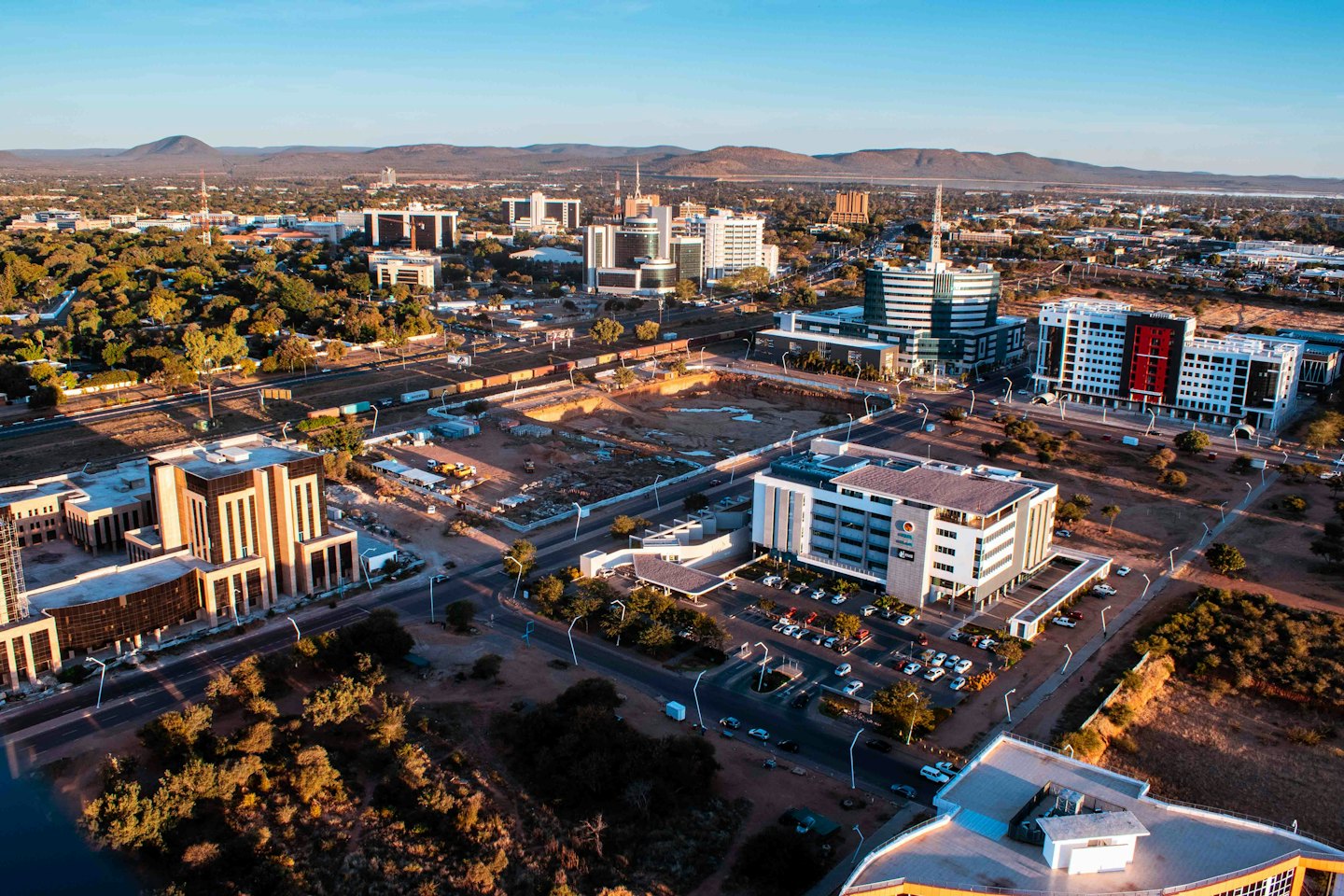 Modern city skyline with red and black buildings near mountains.