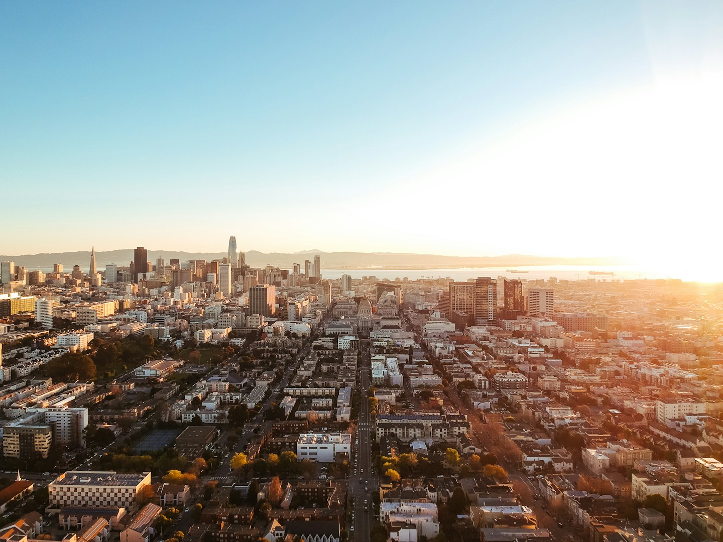 Aerial view of a city skyline at sunset with water and mountains.