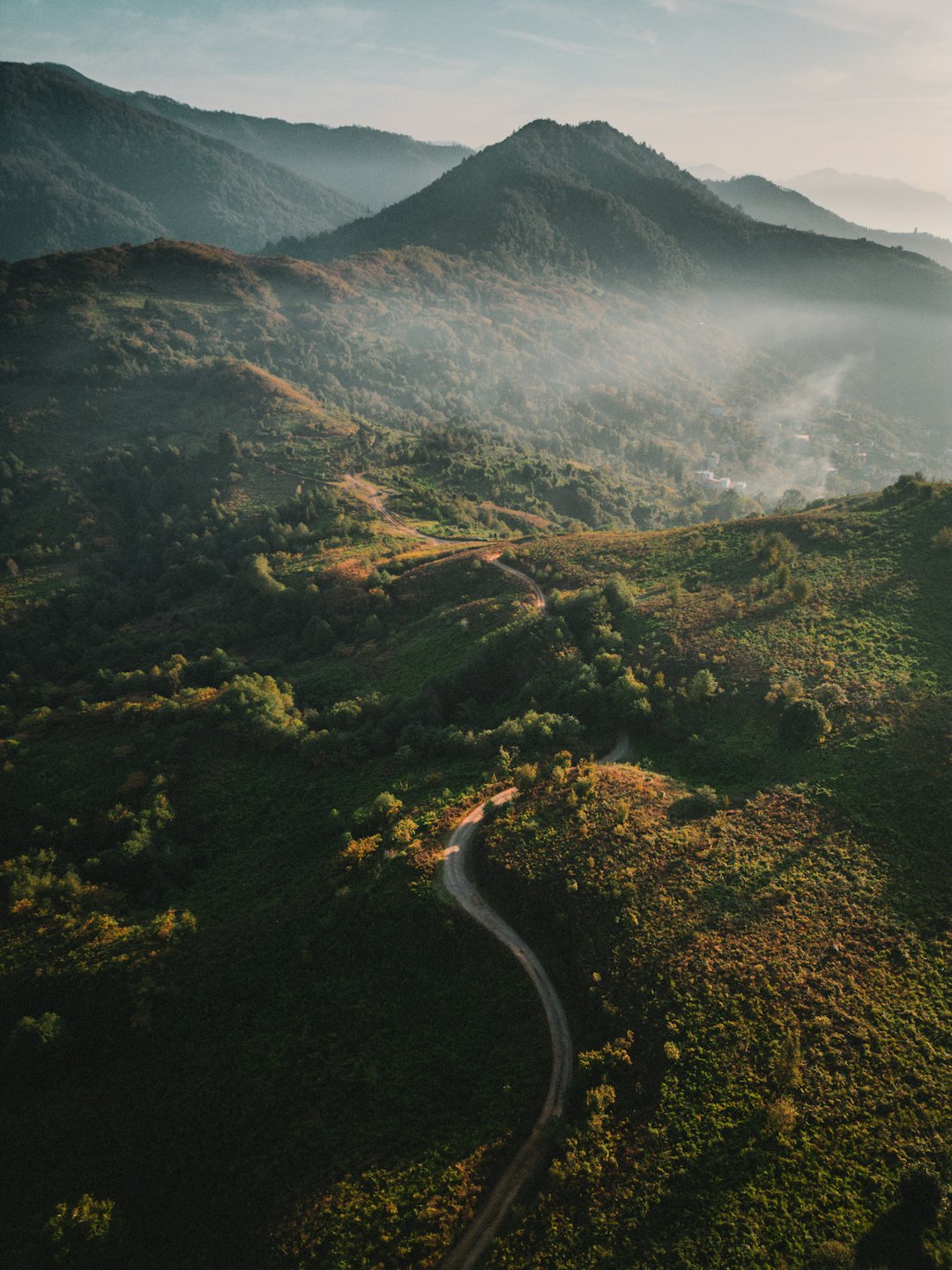 Winding dirt road through lush mountain terrain at sunrise.