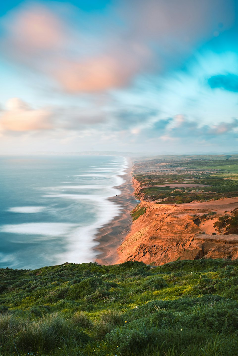 Aerial view of a sandy beach next to reddish-brown cliffs at sunset.