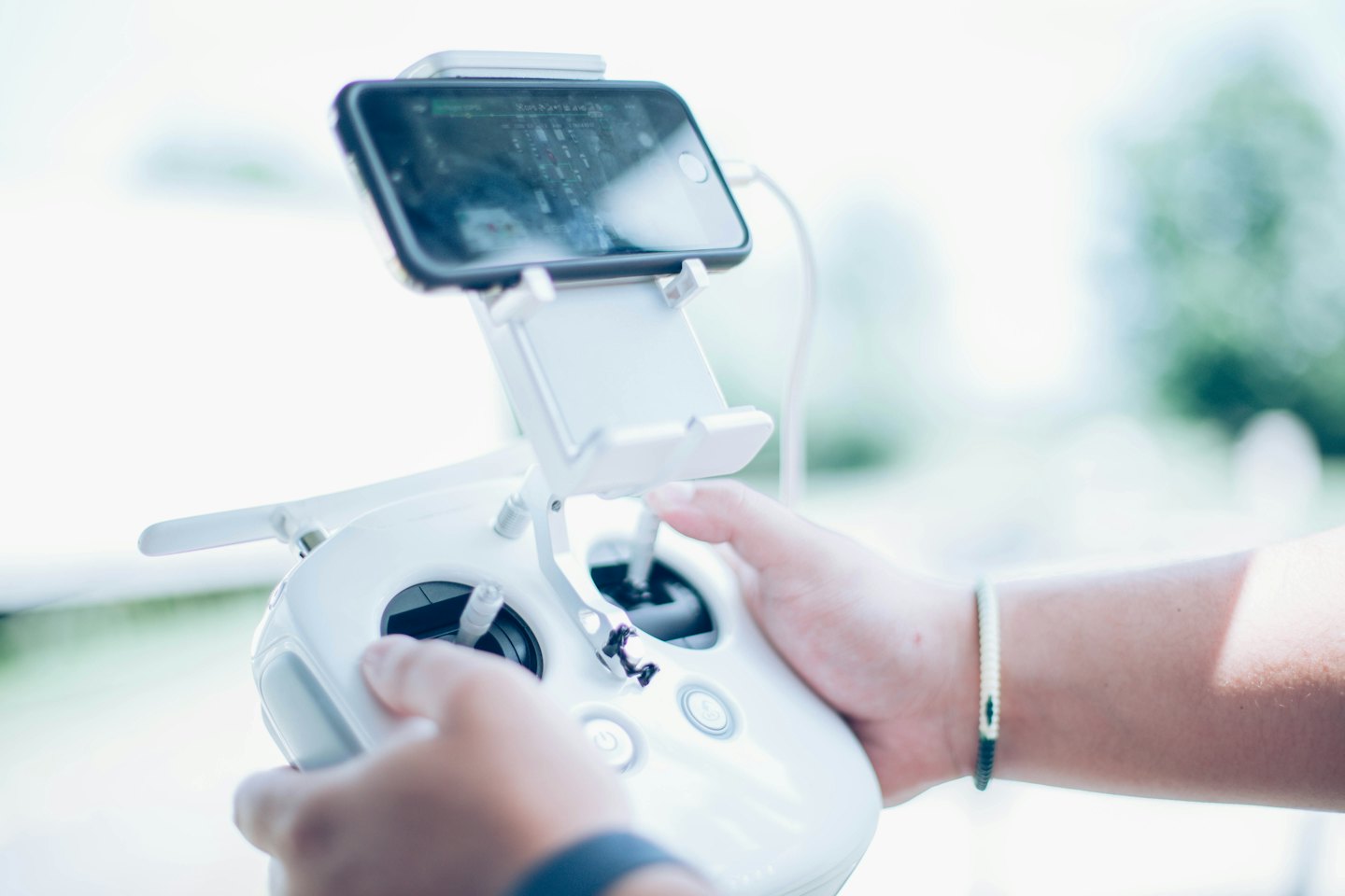 Person's hands controlling a white drone remote with a phone.